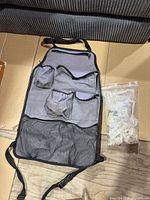 Full view of gray backseat organizer laid flat next to sealed bag of white plastic hardware