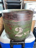 Front view of green metal drum footstool showing stencilled '2 ST' and vinyl cushion