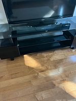 Front view of black glass TV stand with TV on top