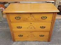 Front view showing three drawers, carvings, hardware, scalloped base