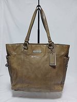 Front view of tan Coach patent leather tote with straps and hangtag