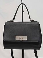 Front view of black saffiano leather satchel showing flap, silver push-lock clasp, top handle, and partial strap