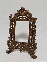 front view of gilt rococo cast metal frame showing cherub crest, scrolling design and missing right top piece