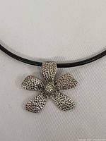 Front view close-up of hammered silver flower pendant on black cord