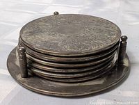Stack of six engraved silver-plated coasters in holder