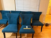 Front view of six teal upholstered chairs showing button-tufted backs and nailhead trim