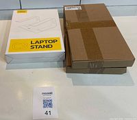 Laptop stand retail box beside sealed brown box containing shoe racks