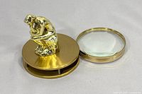 Overall view showing brass statuette atop circular magnifier housing and detached lens