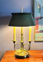 Full view of brass bouillotte lamp with green shade on table, showing overall form and proportions
