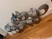Full view showing entire interlocking oval metal sculpture leaning against wall
