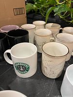 Group shot showing Starbucks mug, ivory gold-rim mugs, black mugs and others