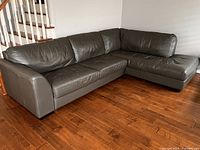 Full view of L-shaped dark grey leather sectional placed against wall
