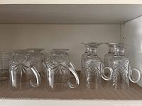 Eight handled cut glass mugs upside down on shelf, focus on shape and cut pattern