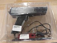 Overall view of black pistol-grip ignition timing light in plastic packaging with attached wires and red inline module