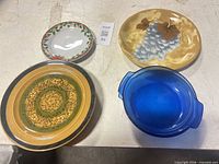 Top view of four representative items: holly plate, grape plate, one dinner plate, one blue baking dish