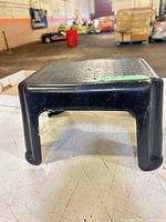 Full view of black plastic step stool showing overall form and wear