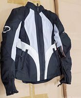 Front view of Daymak women’s textile motorcycle jacket showing color scheme, zippers, waist straps and attached hang tag