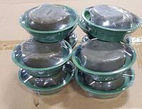 Stack of ten green round wet floral foam forms in green plastic bowls, some fully sealed, some partially unsealed