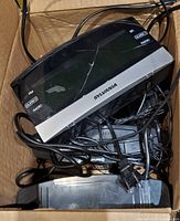 Top view of multiple Sylvania SCR100 clock radios tangled with power cords inside box; crack visible on one front panel