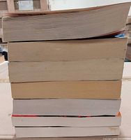 Side view of seven stacked paperback books showing varying thickness and page toning