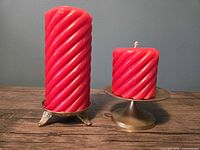 Tall and short red spiral candles on brass holders, side profile