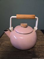 Front view of pink enamel tea kettle showing body, lid, wood handle, spout whistle