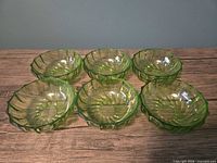 Top view of six light green glass bowls arranged in two rows showing swirl pattern and scalloped rims