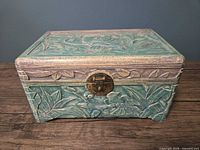 Front view of carved teal wooden box showing latch and floral relief
