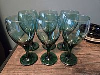 Front angled view of six matching dark green stemmed glasses