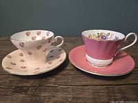 Both Aynsley teacup and saucer sets side by side