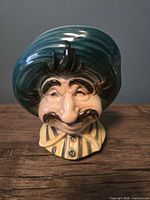 Front view of ceramic man head planter showing facial features, hat, shirt