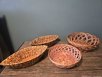 Four baskets on tabletop: two elongated seagrass with wood inserts, one round reed, one round open-lattice wicker