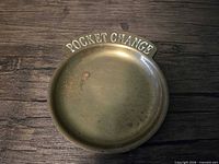 Front view of brass dish showing raised “POCKET CHANGE” lettering and patina