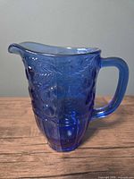 Front view of cobalt blue glass juice pitcher showing fruit embossing and handle