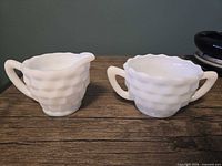 Front view of creamer and sugar bowl showing basketweave pattern and handles