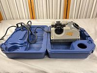 Sharpener seated in open blue case showing power cord and fitted interior