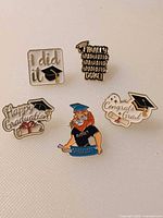 Five graduation enamel pins arranged on white surface
