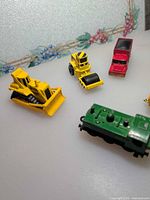 Group shot showing bulldozer, road roller, red truck, green locomotive