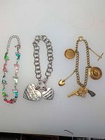 All three bracelets laid out: enamel boot bracelet, heart charm bracelet, western charm bracelet