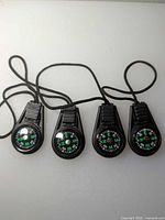 Four identical black plastic compasses with green dials and black cords displayed side by side
