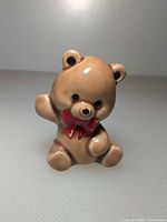 Front view of small ceramic teddy bear figurine with red bow