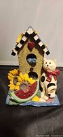 Front view showing entire figurine with cat, birdhouse, sunflowers and watermelon