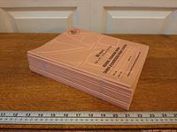 Stack of twelve peach exercise books side view on table with ruler for scale