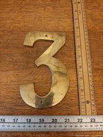Front view brass number 3 alongside rulers showing size