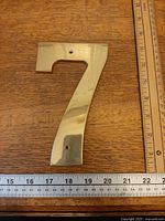 Front view of brass number 7 on wood background with ruler for scale