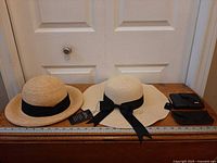 Two raffia hats with tags, two black leather wallets on wood surface