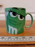 Front view of green Ms. Green character mug with measuring scale
