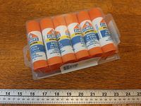 Front view of sealed 12-pack glue sticks with ruler for scale