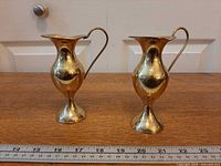 Front view of both brass pitchers next to ruler