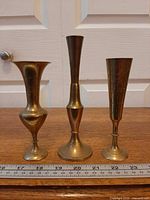 Front view of three brass bud vases with ruler for scale